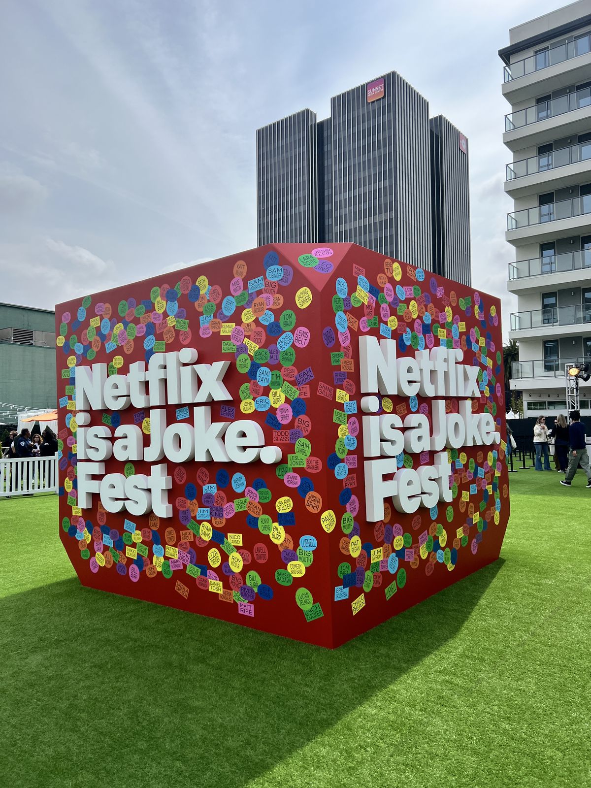 Giant red sculptural cube covered in colorful name stickers on a lawn